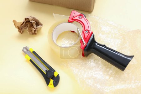 Photo for Packing tape dispenser, utility knife, bubble wrap and crumpled paper on yellow background - Royalty Free Image