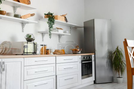 Innenraum der hellen Küche mit stilvollem Kühlschrank, Arbeitsplatten und Regalen