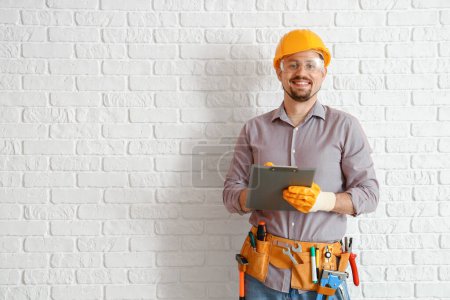 Téléchargez les photos : Constructeur masculin avec presse-papiers près du mur de briques blanches - en image libre de droit