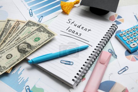 Notizbuch mit Text STUDENT LOANS, Dollarnoten, Graduiertenmütze, Diagrammen und Schreibwaren auf dem Tisch
