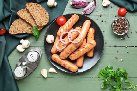 Plate with tasty sausages, bread and vegetables on green wooden table