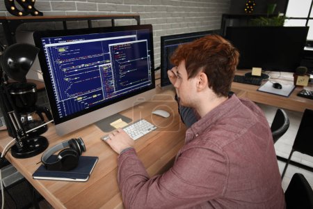 Téléchargez les photos : Programmeur masculin travaillant avec l'ordinateur à la table dans le bureau - en image libre de droit