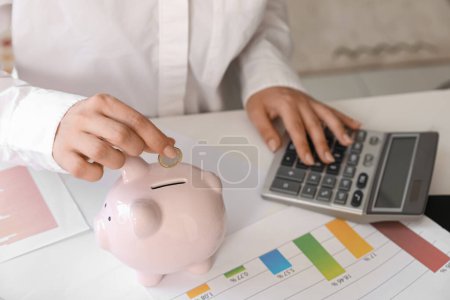 Foto de Estudiante calculando sus finanzas y poniendo moneda en alcancía. Concepto de préstamo estudiantil - Imagen libre de derechos
