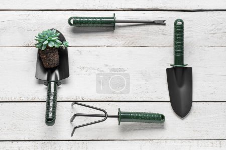 Photo for Frame made of gardening rake, weeder and shovels with plant on white wooden background - Royalty Free Image