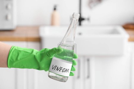 Téléchargez les photos : Main féminine en gant de caoutchouc avec bouteille de vinaigre dans la cuisine - en image libre de droit