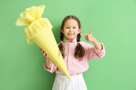 Little girl pointing at yellow school cone on green background