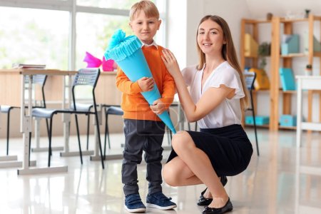 Happy little boy with blue school cone and teacher in classroom