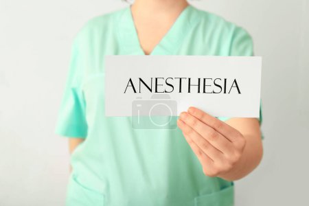Foto de Médico femenino sosteniendo papel con palabra ANESTESIA sobre fondo claro, primer plano - Imagen libre de derechos