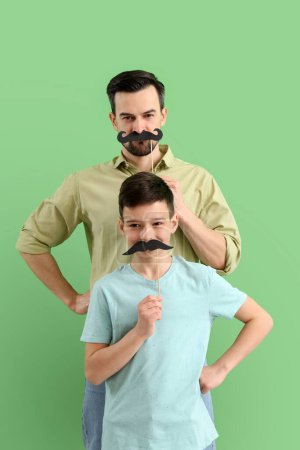 Photo for Portrait of father and his little son with paper mustache on green background - Royalty Free Image
