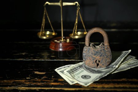 Foto de Cerradura con billetes de dólar y balanzas de justicia en mesa de madera oscura, primer plano. Concepto de sanciones - Imagen libre de derechos
