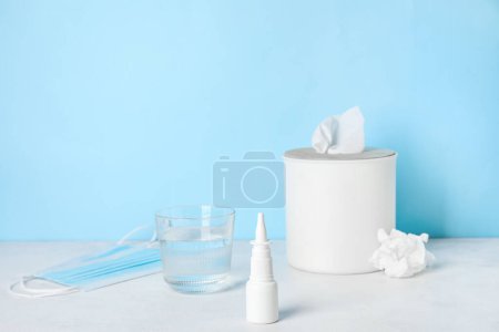 Photo for Nasal drops with glass of water, medical mask and tissue box on table near blue wall. Allergy concept - Royalty Free Image