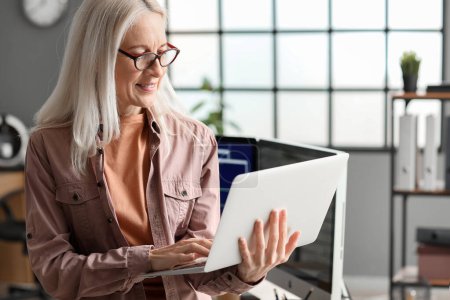 Téléchargez les photos : Femme mature programmeuse travaillant avec un ordinateur portable au bureau - en image libre de droit