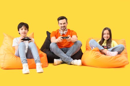 Téléchargez les photos : Père avec ses petits enfants jouant au jeu vidéo sur fond jaune - en image libre de droit