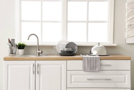 Téléchargez les photos : Comptoir de cuisine avec évier, vaisselle propre et cloche près de la fenêtre - en image libre de droit