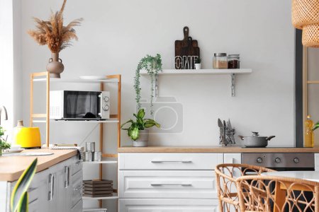 Photo for Interior of modern kitchen with white counters and microwave oven on shelving unit - Royalty Free Image