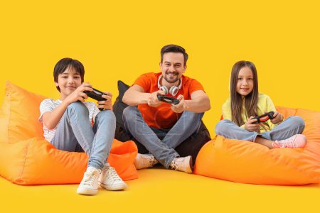 Téléchargez les photos : Père avec ses petits enfants jouant au jeu vidéo sur fond jaune - en image libre de droit