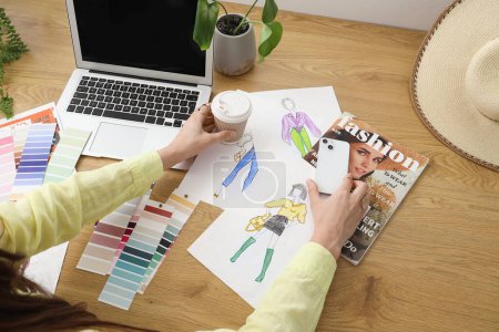 Téléchargez les photos : Créateur de mode travaillant à table avec téléphone portable, tasse de café, échantillons de couleur et ordinateur portable - en image libre de droit