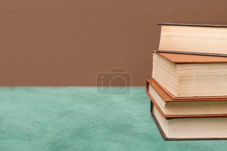 Photo for Stack of books on green table against brown background - Royalty Free Image