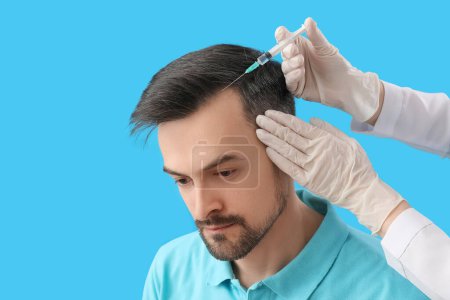 Beau homme recevant l'injection pour la croissance des cheveux sur fond bleu, gros plan