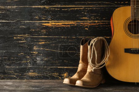 Cowboy boots, guitar and lasso on wooden background