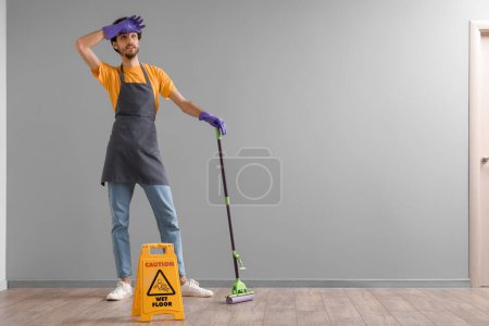 Photo for Tired young man mopping floor near grey wall - Royalty Free Image