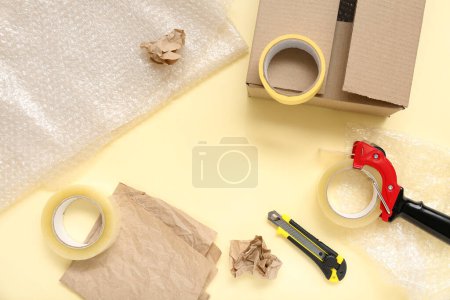 Photo for Composition with packing tape dispenser, utility knife and paper on yellow background - Royalty Free Image