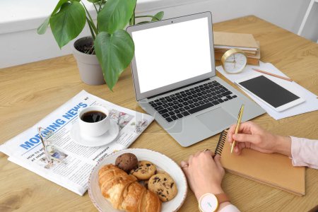 Téléchargez les photos : Femme travaillant à table avec ordinateur portable, tasse de café, collations et carnet - en image libre de droit