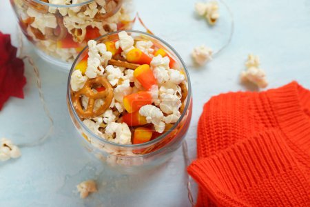 Glas mit leckerem Popcorn, Zuckerhühnern und Brezeln auf weißem Hintergrund, Nahaufnahme. Halloween-Feier