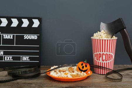 Téléchargez les photos : Composition avec popcorn savoureux, clapperboard, bobine de film et hache sur table en bois. Fête d'Halloween - en image libre de droit