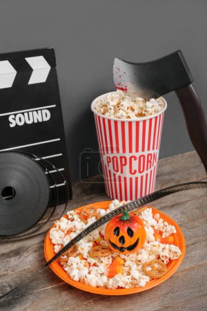 Téléchargez les photos : Composition avec popcorn savoureux, clapperboard, bobine de film et hache sur table en bois. Fête d'Halloween - en image libre de droit