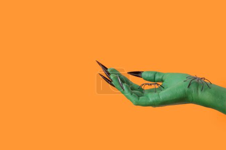 Téléchargez les photos : Main verte de sorcière avec des araignées sur fond orange. Fête d'Halloween - en image libre de droit