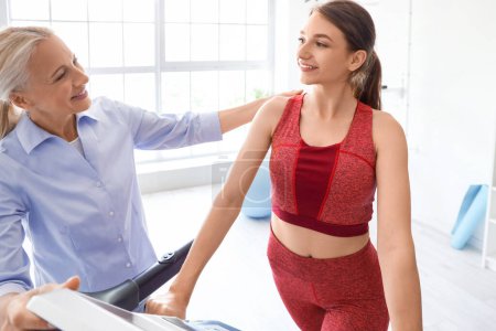 Young woman training with female physiotherapist on treadmill in rehabilitation center