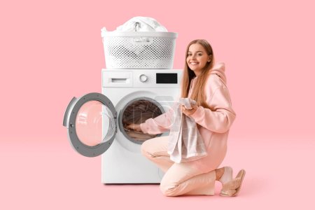Hübsche junge Frau legt schmutzige Wäsche in Waschmaschine auf rosa Hintergrund