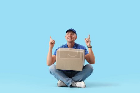 Photo for Mature courier with parcel pointing at something on blue background - Royalty Free Image