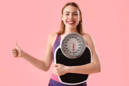 Photo for Sporty young woman with scales showing thumb-up on pink background - Royalty Free Image
