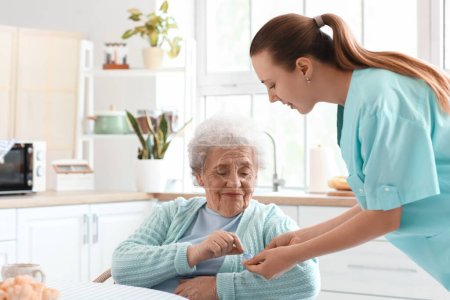 Foto de Cuidador femenino dando pastillas a una mujer mayor en la cocina - Imagen libre de derechos