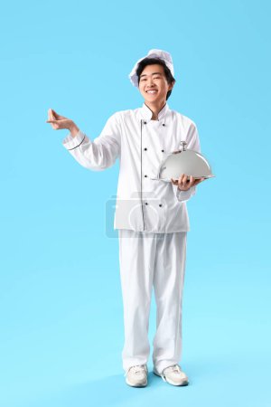 Téléchargez les photos : Homme asiatique chef avec cloche geste sur fond bleu - en image libre de droit