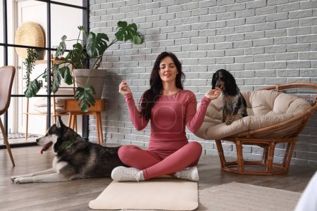 Foto de Mujer joven deportiva con sus perros meditando en casa - Imagen libre de derechos