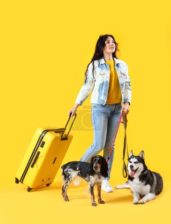 Foto de Mujer joven con lindos perros y maleta sobre fondo amarillo - Imagen libre de derechos