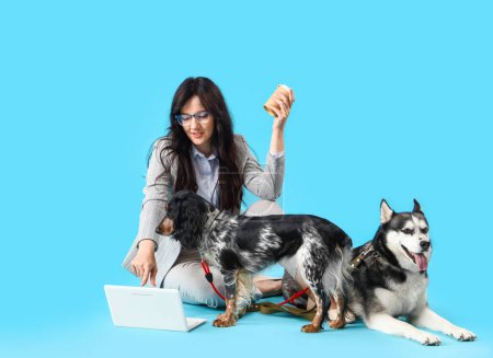 Foto de Joven empresaria con café, perros lindos y portátil sobre fondo azul - Imagen libre de derechos