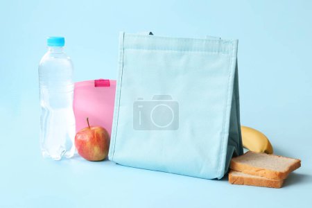 Téléchargez les photos : Sac, boîte à lunch avec de délicieux aliments et bouteille d'eau sur fond bleu - en image libre de droit