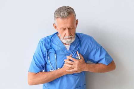 Photo for Mature doctor having heart attack on light background - Royalty Free Image