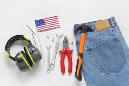 Foto de Composición con diferentes herramientas, orejeras, jeans y bandera de Estados Unidos sobre fondo blanco. Fiesta del Día del Trabajo - Imagen libre de derechos