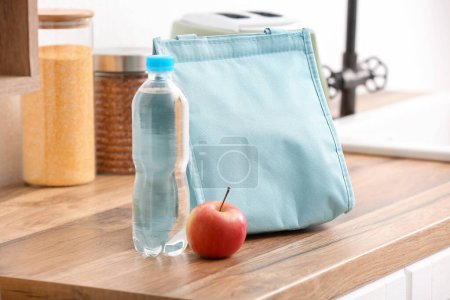 Téléchargez les photos : Sac de déjeuner avec pomme et bouteille d'eau sur la table dans la cuisine - en image libre de droit