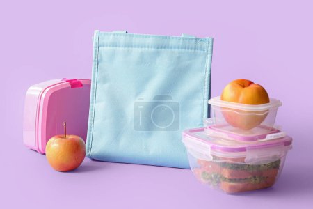 Téléchargez les photos : Sac, boîtes à lunch avec de délicieux aliments et fruits sur fond lilas - en image libre de droit