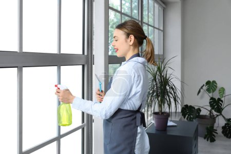 Photo for Female janitor cleaning window with squeegee in office - Royalty Free Image