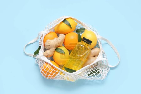 Téléchargez les photos : Sac en filet avec citrons frais, oranges, gingembre et bouteille de jus sur fond bleu - en image libre de droit
