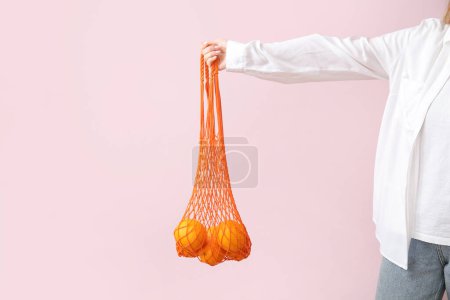 Téléchargez les photos : Sac main femme en mesh avec des oranges fraîches sur fond beige - en image libre de droit