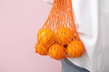 Téléchargez les photos : Femme avec des oranges fraîches dans un sac en filet sur fond beige, gros plan - en image libre de droit
