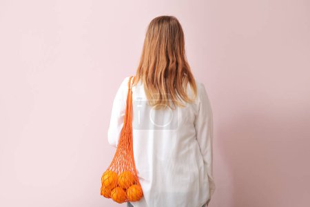 Téléchargez les photos : Femme avec des oranges fraîches dans un sac en filet sur fond beige, vue de dos - en image libre de droit